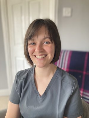 veterinary surgeon with brown hair and grey scrub top smiling